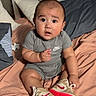 baby, child, sitting, bed, sneakers, nike, gray_clothing, red_sole, curious_expression, indoors, pillow, headboard, blanket, footwear, infant, cute, room, person, portrait, young_child