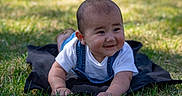 Akani joined the competition — help win amazing prizes! baby, black_cloth, child, cute, denim_overalls, earrings, face, grass, greenery, happy, infant, lying_down, nature, outdoor, portrait, skin, smiling, sunlight, toddler, white_shirt