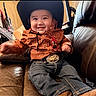 child, toddler, cowboy_hat, orange_shirt, jeans, belt_buckle, leather_couch, smiling, indoor, happy, baby, western_style, cute, portrait, sitting, clothing, person, hat, casual, young