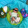 baby, sunglasses, inflatable_ring, toy_ball, bottle, blue_background, baby_clothes, socks, infant, indoor, playtime, colorful, relaxing, cute, child, fun, summer_theme, plastic, bright_colors, accessories
