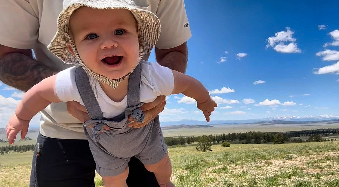 August is registered to the contest to win money with this photo: baby, baby_toddler_clothing, cap, child, cloud, facial_expression, fun, gesture, grass, happy, hat, headwear, leisure, people_in_nature, person, plant, sky, smile, summer, sun_hat