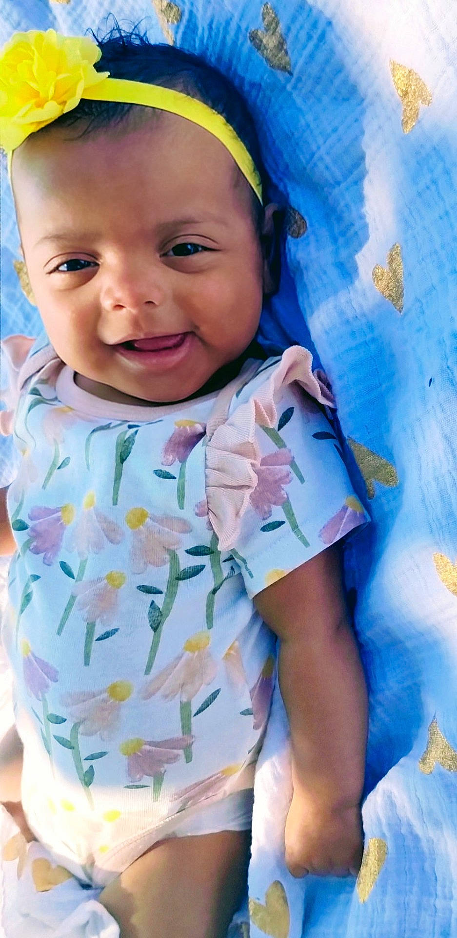 Naxa Sage is registered to the contest to win money with this photo: baby, blanket, blue_blanket, child, closeup, cute, floral_pattern, flower, golden_hearts, hand, happy, headband, infant, laying_down, onesie, portrait, skin, smiling, soft_lighting, young_child