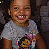 child, toddler, smiling, happy, portrait, curly_hair, brown_eyes, indoors, sitting, gray_shirt, cartoon_shirt, dora_the_explorer, stuffed_toy, television, living_room, furniture, home, closeup, natural_expression, family_photo