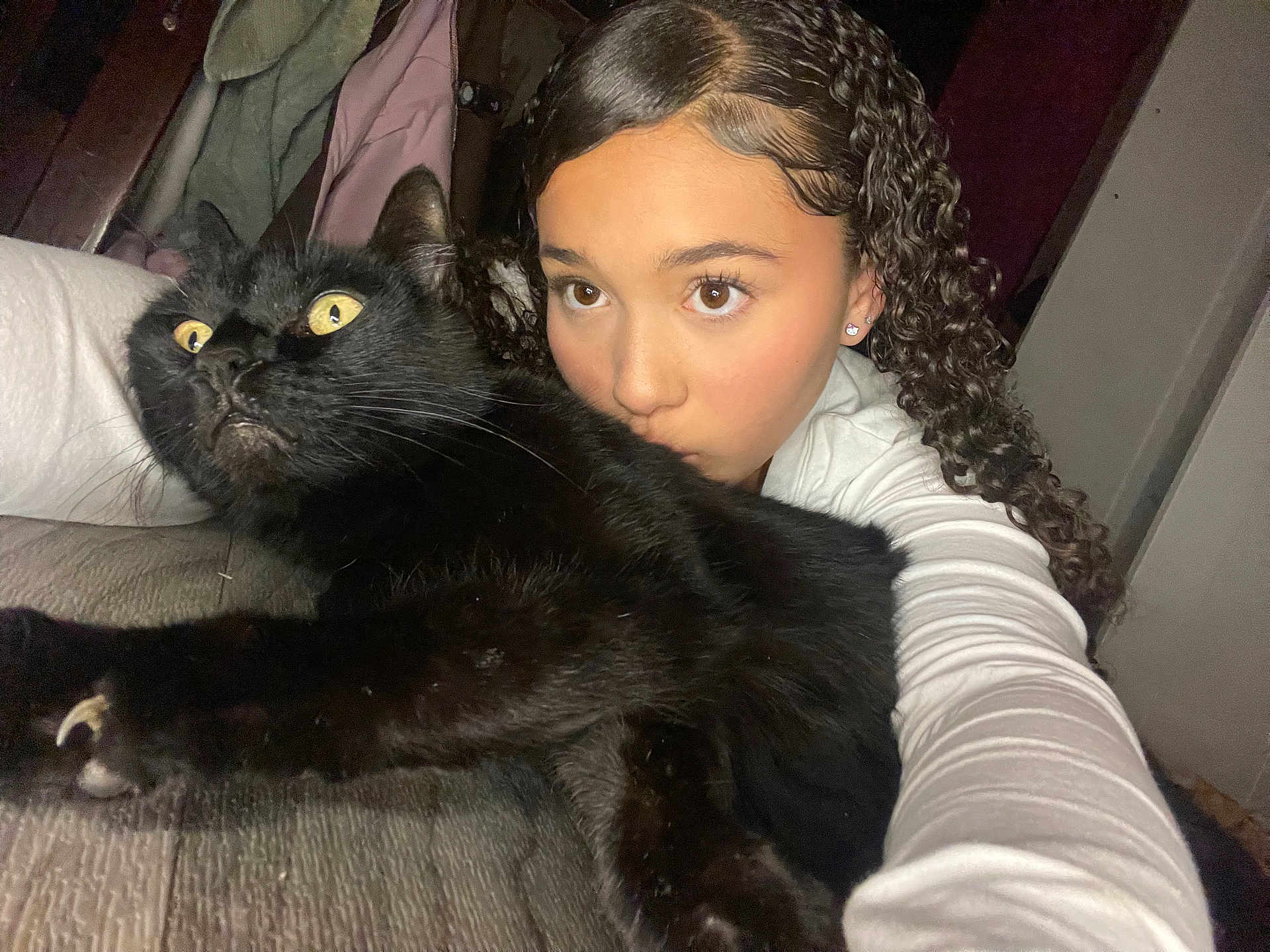 Nieko is registered to the contest to win money with this photo: girl, cat, black_cat, selfie, curly_hair, indoor, wide_eyes, holding, bed, blanket, young_person, portrait, pet, animal, feline, face, expression, cozy, casual, white_shirt