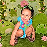 blue_clothing, child, cute, decorations, fairy_lights, fantasy_theme, flowers, frog_toys, green, hair_bows, happy, indoor, lily_pad, lotus, person, playful, plush, shoes, smiling, toddler