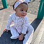 baby, child, infant, headband, bow, onesie, floral_pattern, playground, outdoor, curious, sitting, cute, portrait, sunlight, daylight, skin, hand, footed_pajamas, expression, young