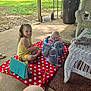 child, toddler, baby, blanket, toy, plush_elephant, porch, wicker_chair, outdoor, grass, sunlight, concrete_floor, smiling, sitting, yellow_clothes, blue_seat, playtime, nature, family, relaxation