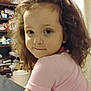 child, curly_hair, pink_shirt, smile, portrait, indoor, person, face, young, casual_clothing, room, shelf, household_items, background, curly_hair_child, looking_back, cute, expression, closeup, soft_lighting