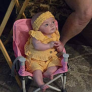 Hailey is registered to the contest to win money with this photo: baby, child, yellow_clothing, headband, pink_chair, indoor, carpet, person, legs, seated, curious, infant, furniture, patterned, footwear_absent, small_chair, cute, baby_girl, soft_lighting, casual