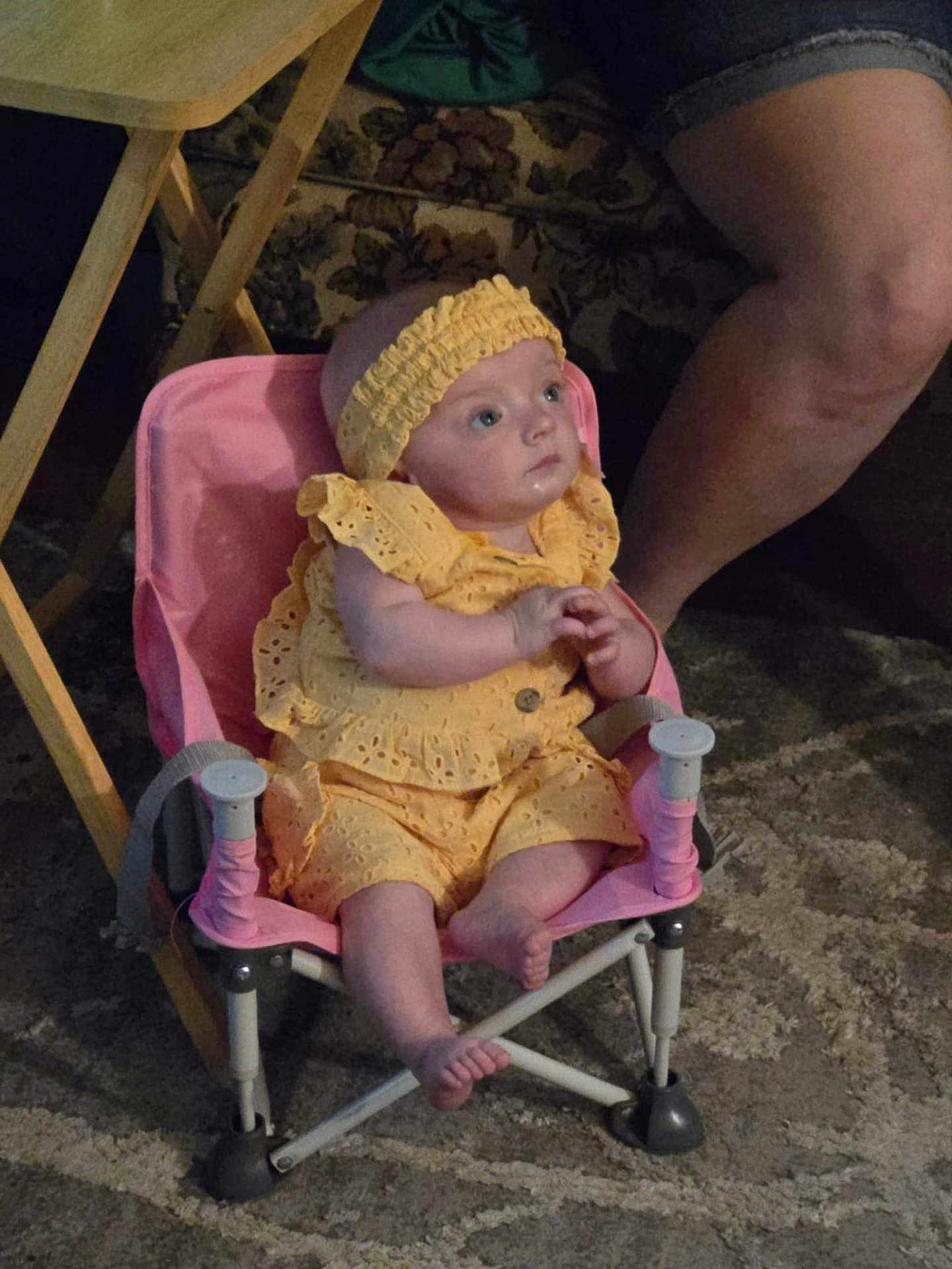 Hailey is registered to the contest to win money with this photo: baby, child, yellow_clothing, headband, pink_chair, indoor, carpet, person, legs, seated, curious, infant, furniture, patterned, footwear_absent, small_chair, cute, baby_girl, soft_lighting, casual