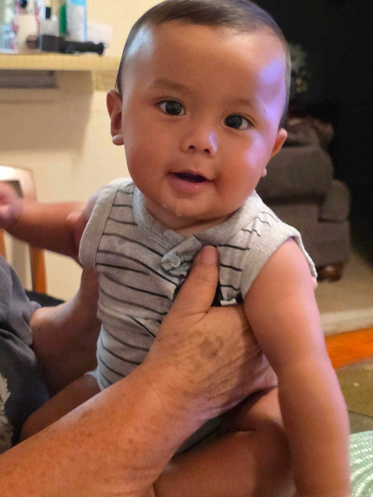 Isaac joined the competition — help win amazing prizes! baby, child, person, indoor, holding, striped_clothing, smiling, cute, arm, hand, furniture, living_room, portrait, skin, head, face, eyes, infant, seated, happy