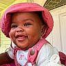 Kulture is registered to the contest to win money with this photo: baby, child, smiling, pink_hat, pink_overalls, white_shirt, happy, face, portrait, indoors, door, decorative_glass, closeup, cute, infant, cheerful, person, clothing, babywear, headwear