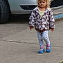 child, sidewalk, car, blond_hair, jacket, leggings, blue_shoes, walking, outdoor, curly_hair, vehicle, person, casual, street, concrete, toddler, daytime, urban, parked_car, curb