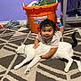 baby, child, cat, white_cat, hugging, floor, carpet, orange_bucket, purple_wall, toy, indoor, smiling, happy, person, animal, pet, cute, relaxed, home, childhood