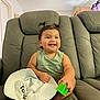 toddler, child, smile, happy, pigtails, green_toy, white_hat, gray_couch, indoor, person, cute, baby, sitting, playful, casual_clothing, furniture, home, portrait, young_child, cheerful