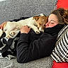 black_clothing, blanket, blanket_fringe, brown_and_white_dog, casual, comfort, couch, cozy, dog, face, furniture, hair, indoor, paw, person, pillow, relaxing, resting, sleeping, snuggling
