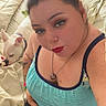 woman, selfie, bed, dog, casual, indoor, clothing, jewelry, tattoo, furniture, dresser, clutter, pet, face, hair_bun, makeup, nose_ring, shorts, blanket, relaxed