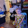 child, girl, toddler, portrait, smiling, sitting, chair, dress, princess, colorful_clothing, blonde_hair, indoor, home, playroom, refrigerator, shelves, storage_bins, laundry, ball, pet_cage