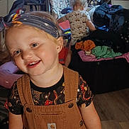 Chole is registered to the contest to win money with this photo: chair, child, clothing, family, furniture, girl, happy, headband, home, indoor, laundry, overalls, playroom, portrait, shelf, smiling, tablet, television, toddler, toys