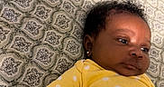 Emori is registered to the contest to win money with this photo: baby, infant, yellow_clothing, polka_dot, earrings, bedspread, patterned_fabric, lying_down, close_up, face, skin, curly_hair, arm, hand, indoor, portrait, child, cute, sleepwear, young