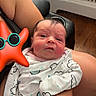 Mariana is registered to the contest to win money with this photo: arm, baby, cloud_pattern, comfort, cute, expression, face, floor, hand, holding, indoor, infant, newborn, onesie, person, resting, skin, starfish_toy, sunglasses, wooden_floor