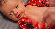 Eva is registered to the contest to win money with this photo: baby, infant, red_clothing, striped_clothing, blanket, bed, lying_down, face, hand, foot, skin, newborn, cute, expression, motion_blur, white_blanket, gray_surface, indoor, child, person