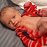 baby, infant, red_clothing, striped_clothing, blanket, bed, lying_down, face, hand, foot, skin, newborn, cute, expression, motion_blur, white_blanket, gray_surface, indoor, child, person