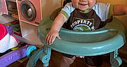 Merle is registered to the contest to win money with this photo: baby, child, clothing, cute, floor, furniture, happy, home, indoor, infant, person, play_kitchen, playtime, room, smiling, standing, toy, walker, wooden_floor, young_child