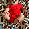 baby, infant, pacifier, red_clothing, football_pattern, blanket, feet, hand, lying_down, cute, child, young_child, indoors, soft_texture, smiling_eyes, cozy, comfort, portrait, closeup, playful