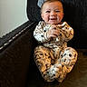 animal_print, baby, chair, child, clapping, clothing, comfort, cushion, cute, expression, face, happy, indoors, infant, pajamas, person, portrait, sitting, smiling, young_child