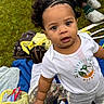 Jamari joined the competition — help win amazing prizes! toddler, child, outdoor, grass, blanket, white_shirt, curly_hair, braided_hair, bag, shoes, camouflage_pants, picnic, playing, person, casual_clothing, expression, young_child, nature, daylight, curiosity