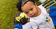 Jamari is registered to the contest to win money with this photo: child, toddler, braided_hair, grass, outdoor, blanket, white_shirt, curious_expression, person, playing, casual, daylight, summer, greenery, camo_pants, footwear, baby, head, cute, portrait