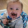 baby, bib, cheerful, child, chocolate, clothing, cute, face, feeding, hair, hand, happy, high_chair, indoors, infant, messy, patterned_clothing, sitting, smiling, wooden_floor