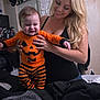 baby, child, woman, smiling, pumpkin_outfit, orange_clothing, striped_pants, indoor, bedroom, hats, figurines, holding, happy, person, portrait, long_hair, casual, home, clothing, joy