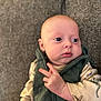 baby, infant, child, face, eyes, hand, fingers, clothing, vest, dinosaur_print, couch, furniture, indoor, portrait, cute, chubby_cheeks, expression, person, sitting, young