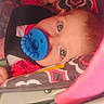 baby, pacifier, car_seat, child, blue_eyes, red_clothing, patterned_fabric, infant, seatbelt, close_up, cute, safety, child_safety_seat, pink, red, baby_girl, baby_boy, indoor, young_child, portrait