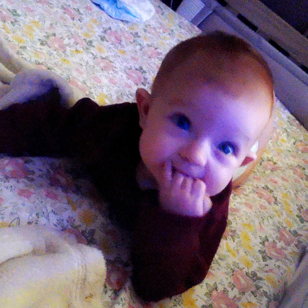 April is registered to the contest to win money with this photo: baby, child, infant, bed, blanket, floral_bedspread, diaper, fingers, hand, face, person, indoors, sleepwear, cute, young, curious, lying, cozy, home, portrait