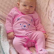 April joined the competition — help win amazing prizes! baby, infant, pink_clothing, onesie, bear_design, blanket, soft_texture, cute, indoor, child, toddler, sleepwear, footed_pajamas, expression, sitting, young_child, person, head, face, skin