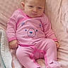 baby, infant, pink_clothing, onesie, bear_design, blanket, soft_texture, cute, indoor, child, toddler, sleepwear, footed_pajamas, expression, sitting, young_child, person, head, face, skin