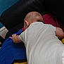Kaïs participe au concours pour gagner de l'argent avec cette photo : arm, baby, baby_clothing, back, black_couch, blanket, blue_wall, colorful_blanket, couch, exploring, fabric, floor, hand, head, indoor, infant, skin, textile, wall, white_onesie