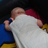 Kaïs participe au concours pour gagner de l'argent avec cette photo : arm, baby, back_view, black, blanket, blue, child, colorful, head, indoors, infant, lying_down, red, resting, skin, soft, toddler, white_onesie, yellow, young