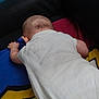 arm, baby, back_view, black, blanket, blue, child, colorful, head, indoors, infant, lying_down, red, resting, skin, soft, toddler, white_onesie, yellow, young
