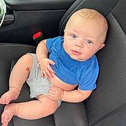 Kaidyn joined the competition — help win amazing prizes! baby, child, car_seat, blue_shirt, gray_shorts, infant, person, cute, skin, legs, feet, hand, seatbelt, car_interior, curious, sitting, young, portrait, casual, relaxed