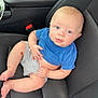 baby, child, car_seat, blue_shirt, gray_shorts, infant, person, cute, skin, legs, feet, hand, seatbelt, car_interior, curious, sitting, young, portrait, casual, relaxed