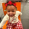 toddler, child, red_bow, smiling, orange_chair, red_checkered_pants, white_shirt, necklace, indoor, happy, cute, face, person, clothing, sitting, feet, socks, playful, joy, portrait