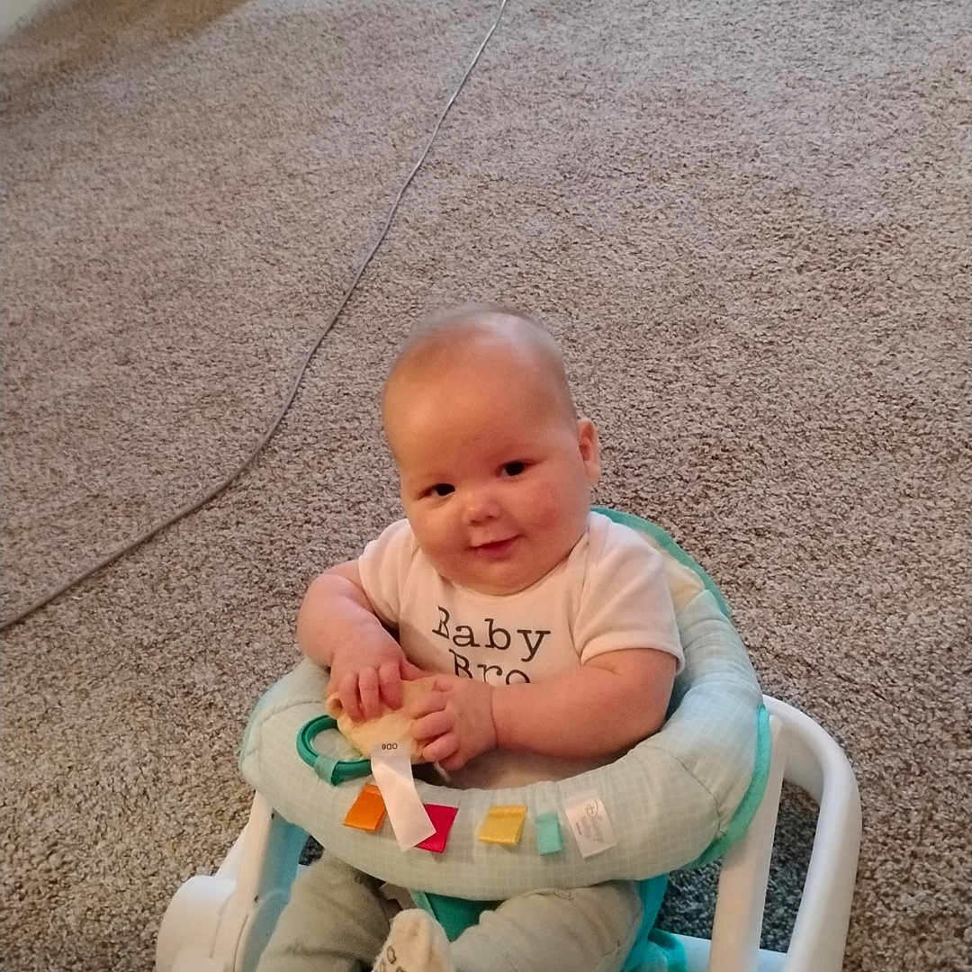 Waylin Seaton joined the competition — help win amazing prizes! baby, child, infant, smiling, sitting, activity_seat, baby_walker, carpet, indoor, living_room, office_chair, charging_cable, toy, rainbow, winnie_the_pooh, clothing, portrait, happy, home, photograph