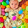 baby, child, easter_eggs, colorful, plastic_eggs, headband, bunny, skirt, infant, cute, face, fist, looking_at_camera, lying_down, soft_lighting, celebration, holiday, pastel_colors, playful, festive