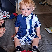 Arlo-Alexander is registered to the contest to win money with this photo: child, toddler, curly_hair, striped_clothing, blue_and_white, sneakers, black_shoes, red_soled_shoes, socks, wooden_floor, indoor, person, sitting, hand, toy, background, shoe, flooring, casual_clothing, curly_blond_hair
