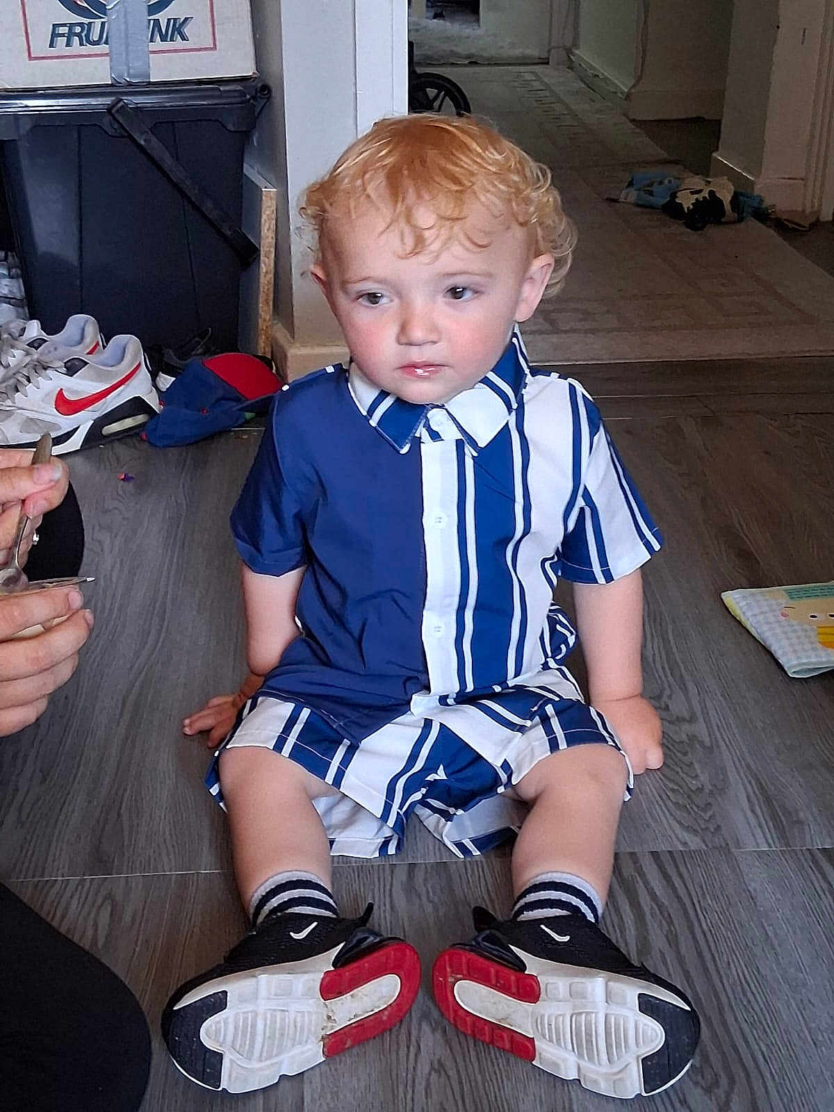 Arlo-Alexander is registered to the contest to win money with this photo: child, toddler, curly_hair, striped_clothing, blue_and_white, sneakers, black_shoes, red_soled_shoes, socks, wooden_floor, indoor, person, sitting, hand, toy, background, shoe, flooring, casual_clothing, curly_blond_hair