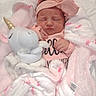 baby, newborn, infant, pink_clothing, headband, plush_toy, unicorn, blanket, pink_blanket, flamingo_pattern, sleeping, cute, soft_texture, cozy, child, portrait, indoors, resting, peaceful, wrapped